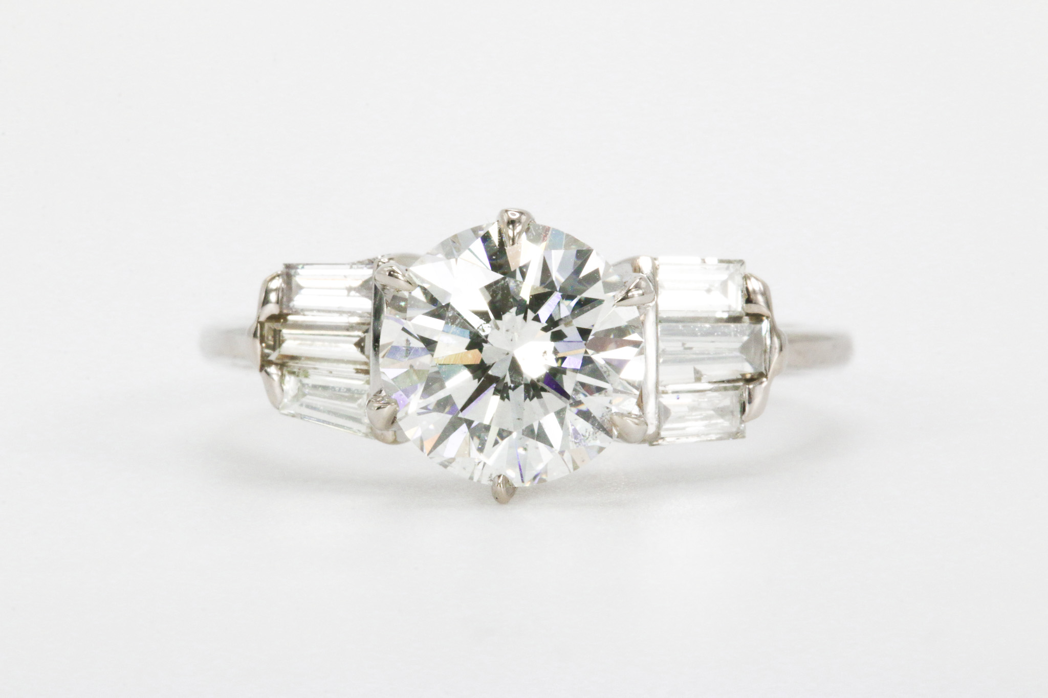 Ring with a large central round diamond and baguette diamonds on each side, set in a metal band.
