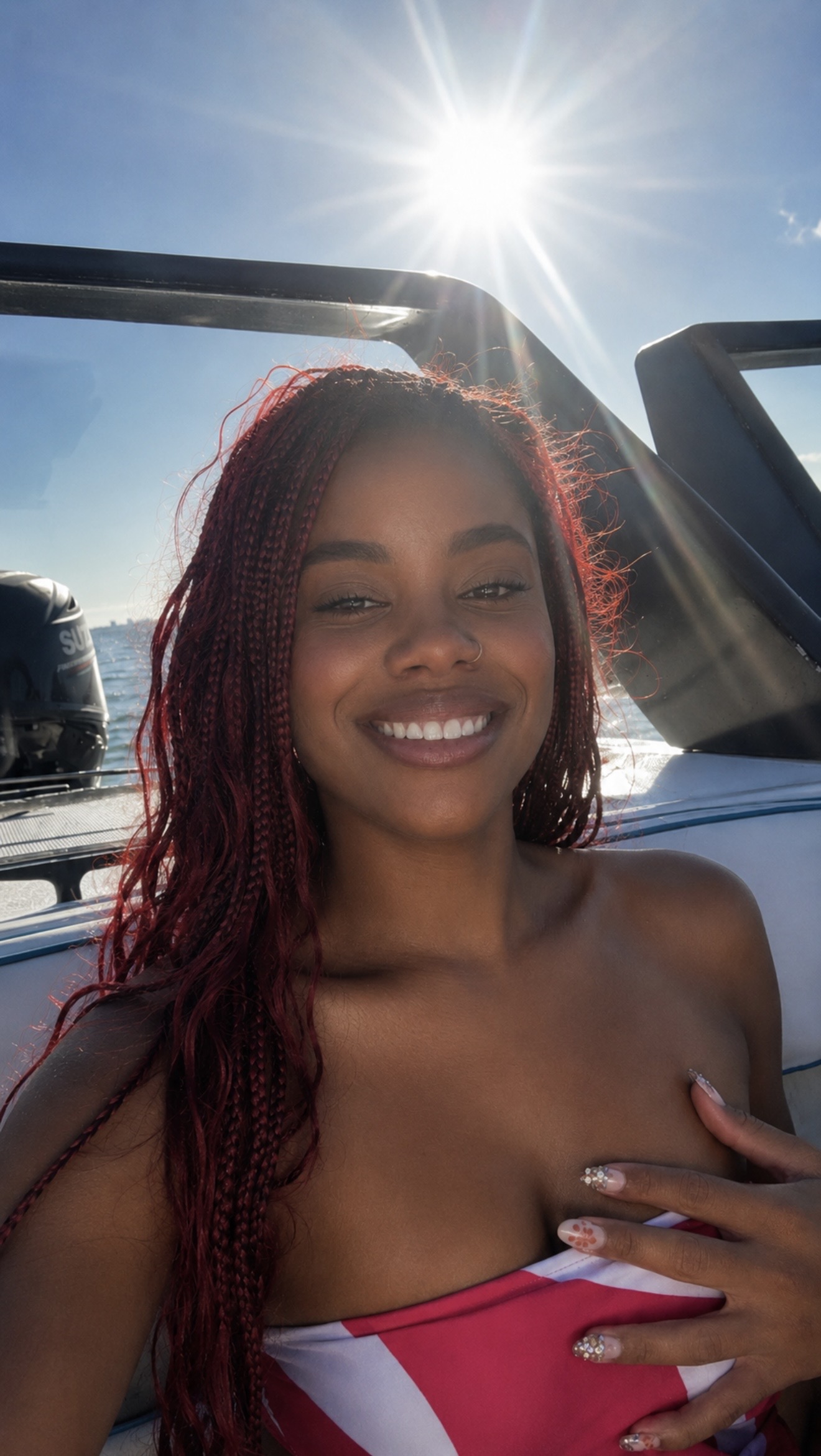 Smiling woman with red hair outdoors, sun shining brightly, in a vehicle with open top, hand on chest.