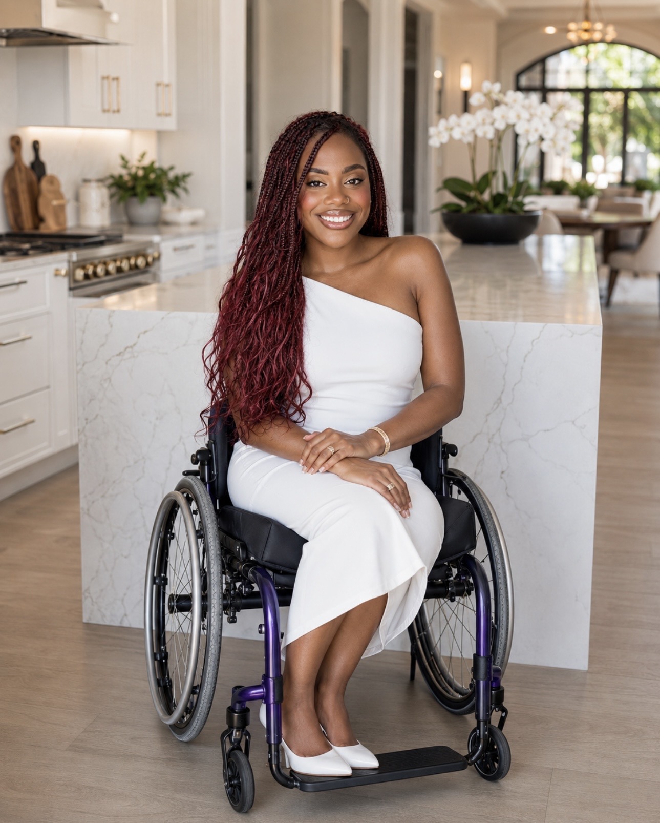 Woman in white dress sitting in a wheelchair in a bright, modern kitchen with plants and large windows.