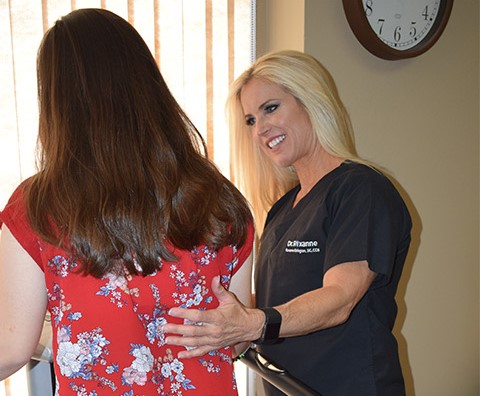 A healthcare professional smiling and talking to a woman with long brown hair in a room with a clock on the wall.