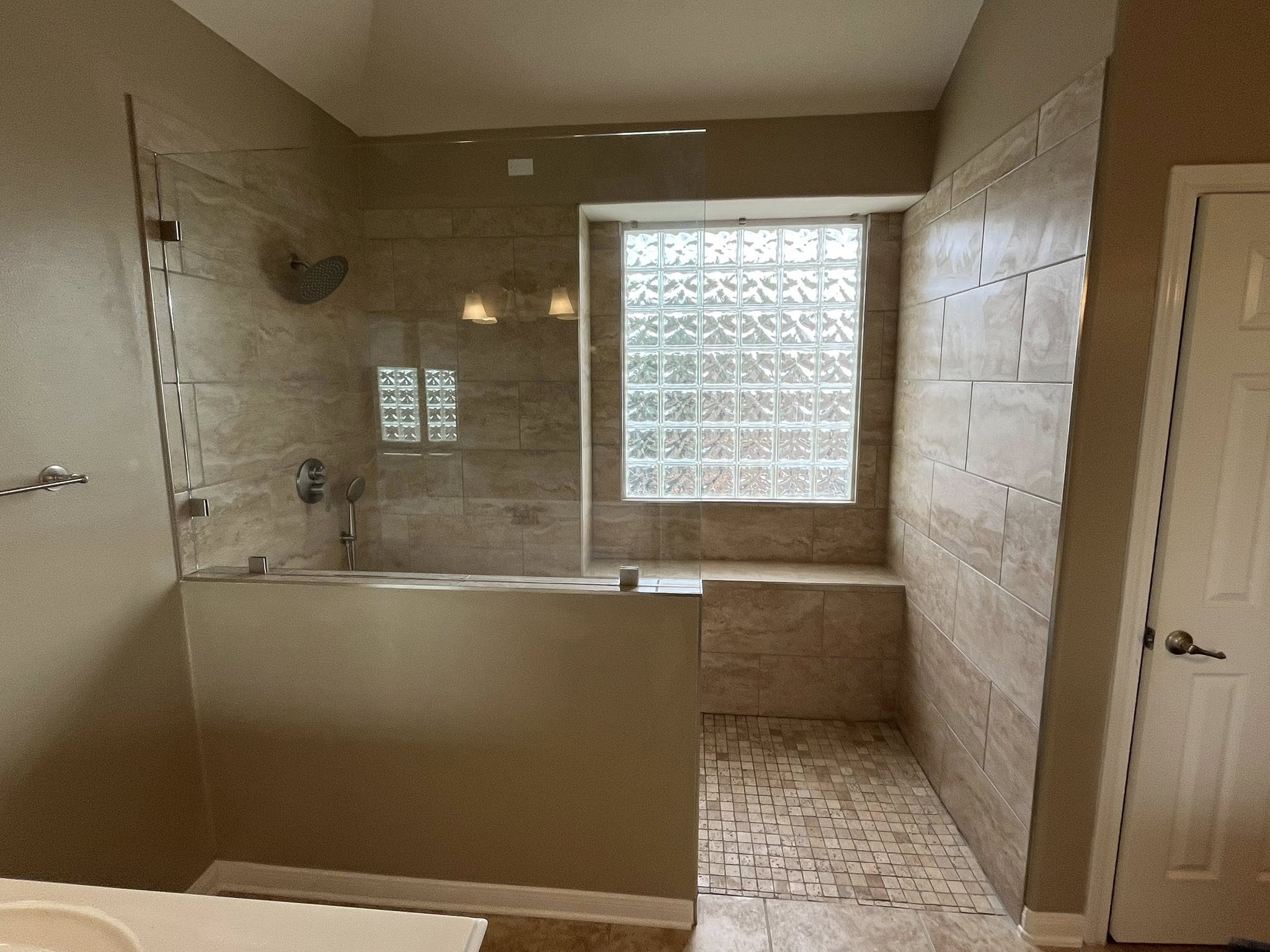 Bathroom with bathtub, glass block window, tiled walls, and a door on the right side.