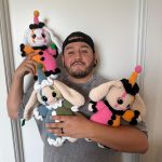 Person holding three colorful knitted animal toys, standing against a plain white wall.