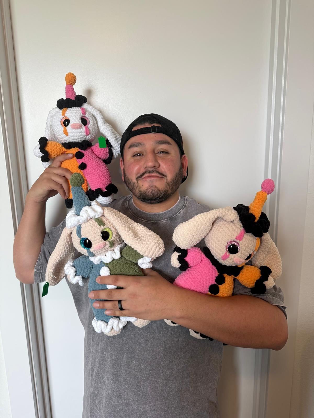 Person holding three colorful knitted animal toys, standing against a plain white wall.