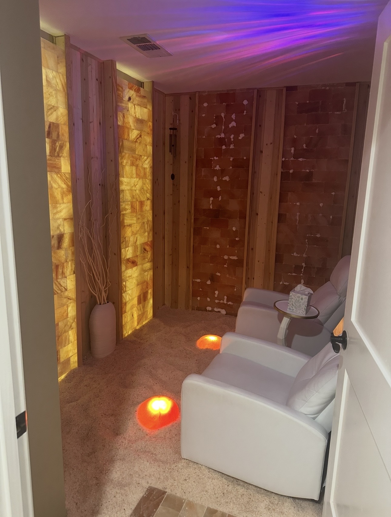 Two white armchairs with pillows in a room with wooden wall panels and decorative lighting, including purple and orange lights.