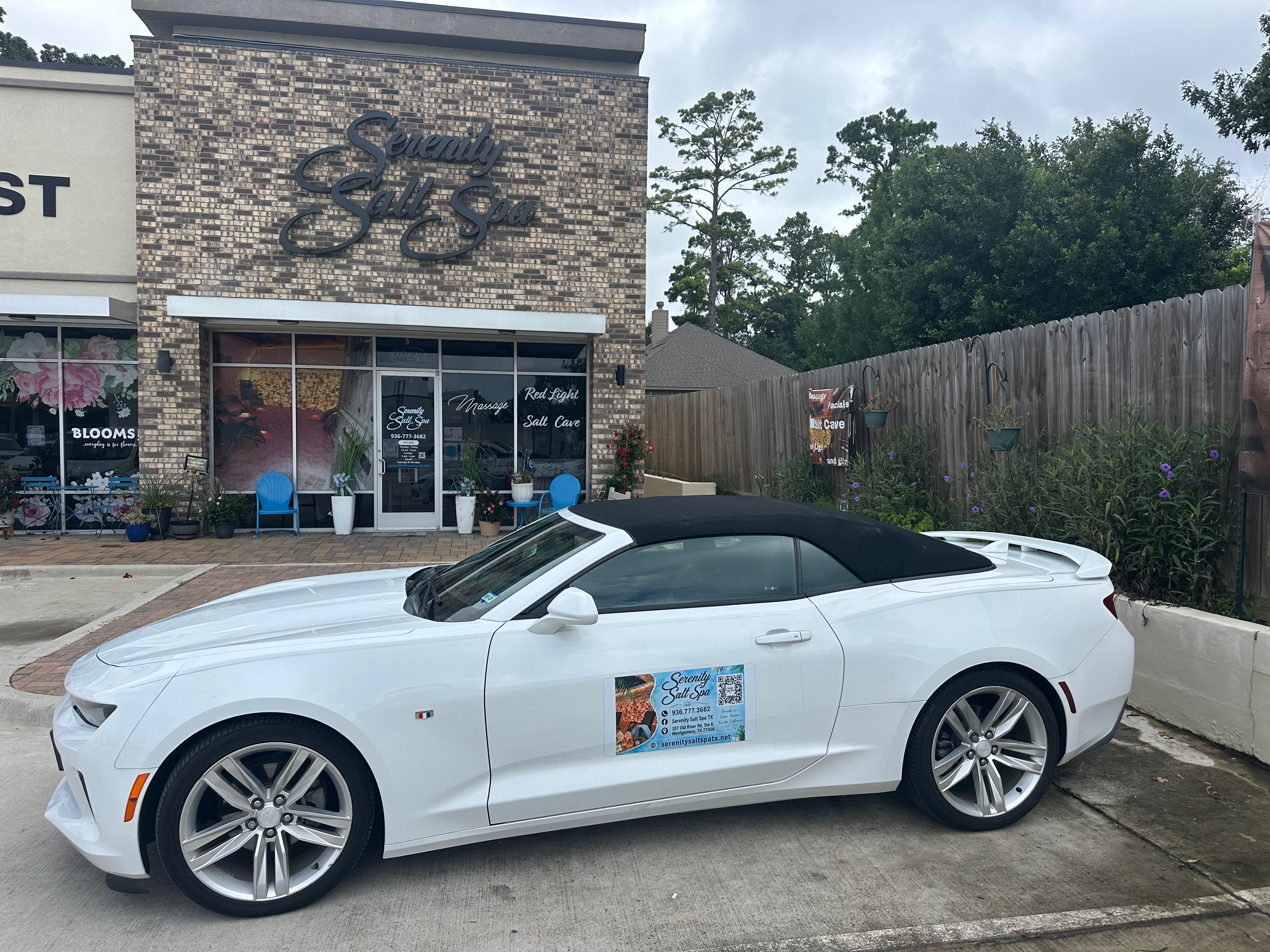 White convertible car parked outside a building with a brick facade and large windows, with a poster on the side.