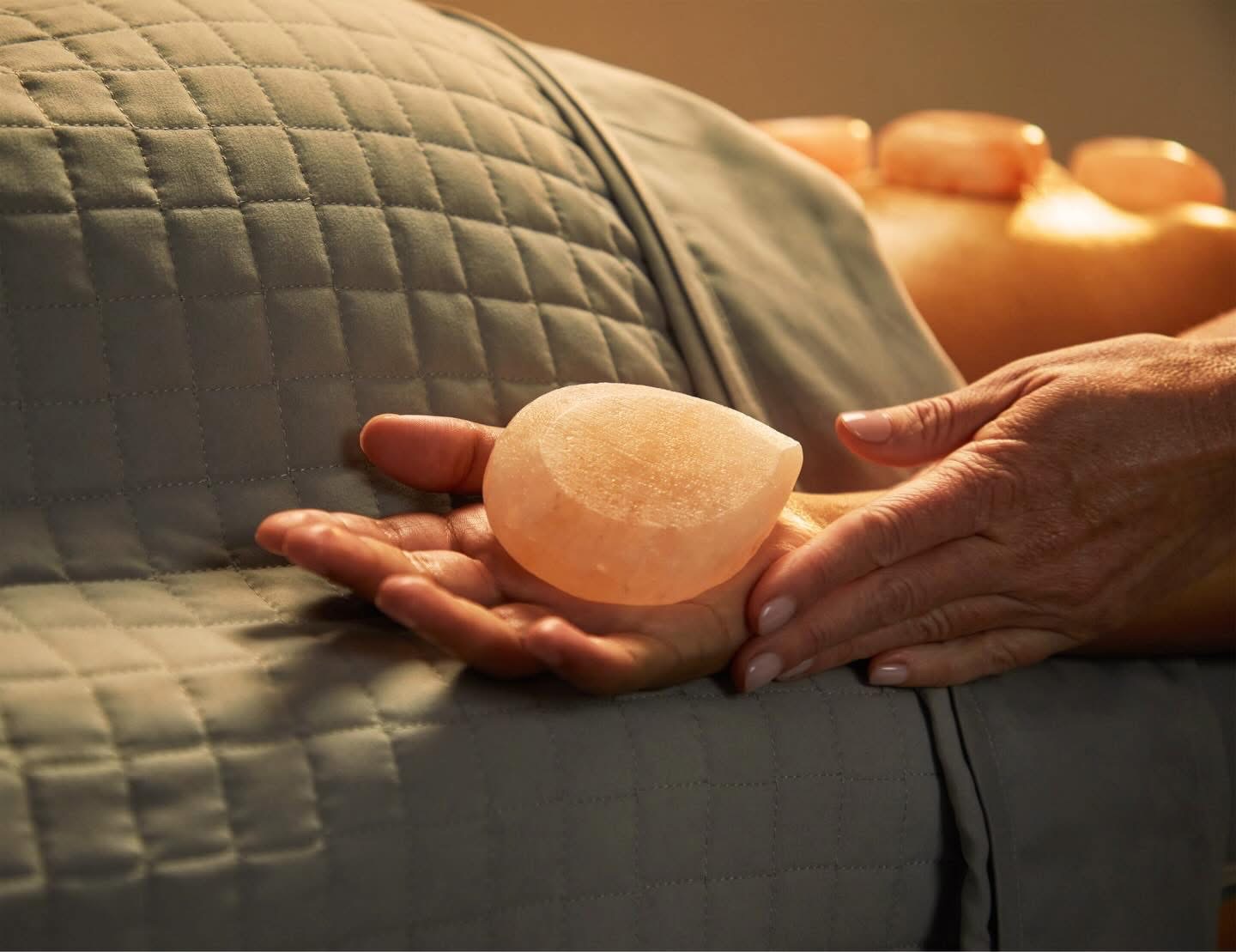 A person holds a salt lamp in their hand, resting on a quilted surface with more salt lamps in the background.