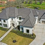 Large modern house with multiple roof sections, front walkway, and attached garage, surrounded by a well-maintained lawn and trees.