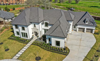 Large modern house with multiple roof sections, front walkway, and attached garage, surrounded by a well-maintained lawn and trees.