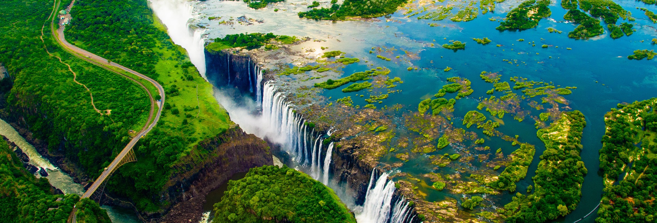 Panoramic view of a waterfall with lush green surroundings and a river with aquatic plants.