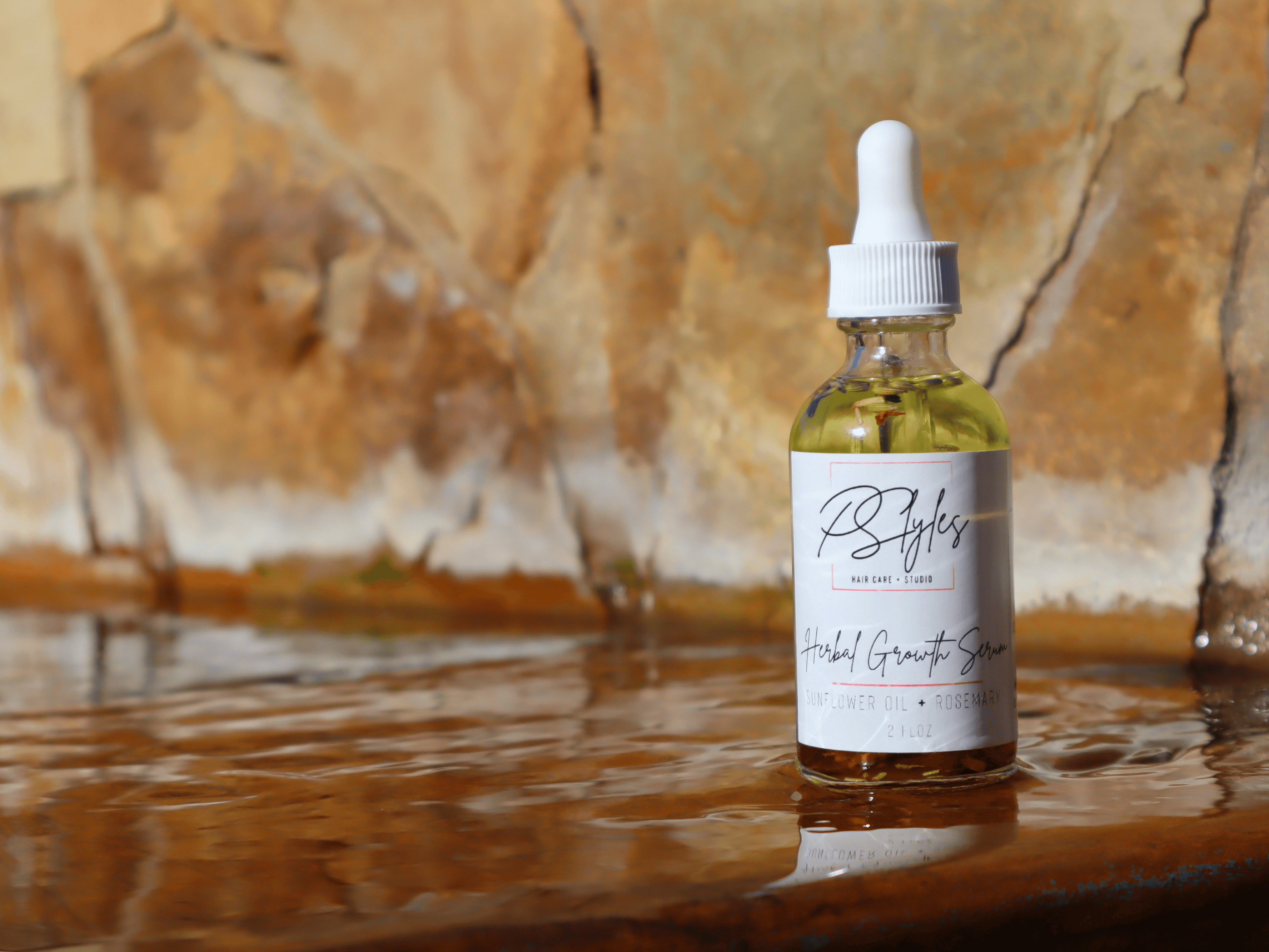 Dropper bottle with a white label and white cap placed on a wet surface with a stone background.