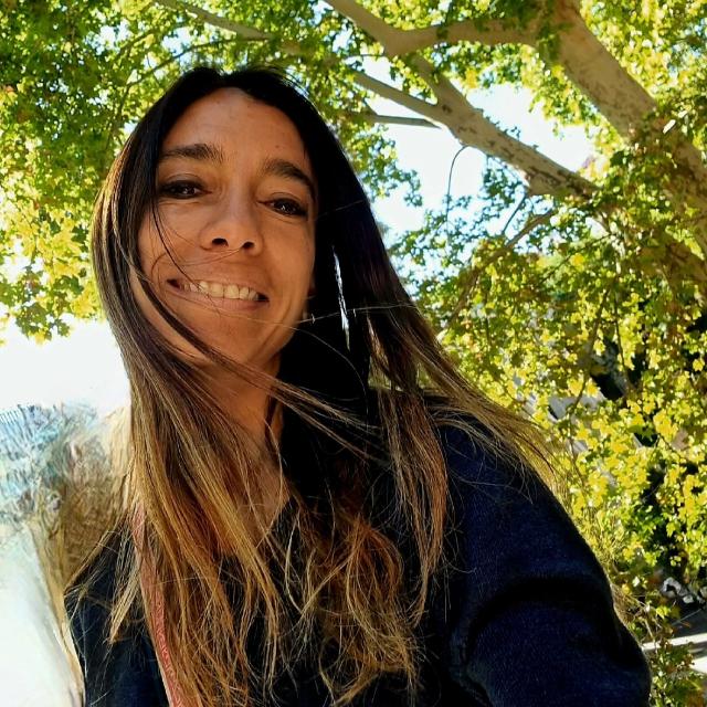 Woman smiling outdoors with green leaves and sunlight overhead.