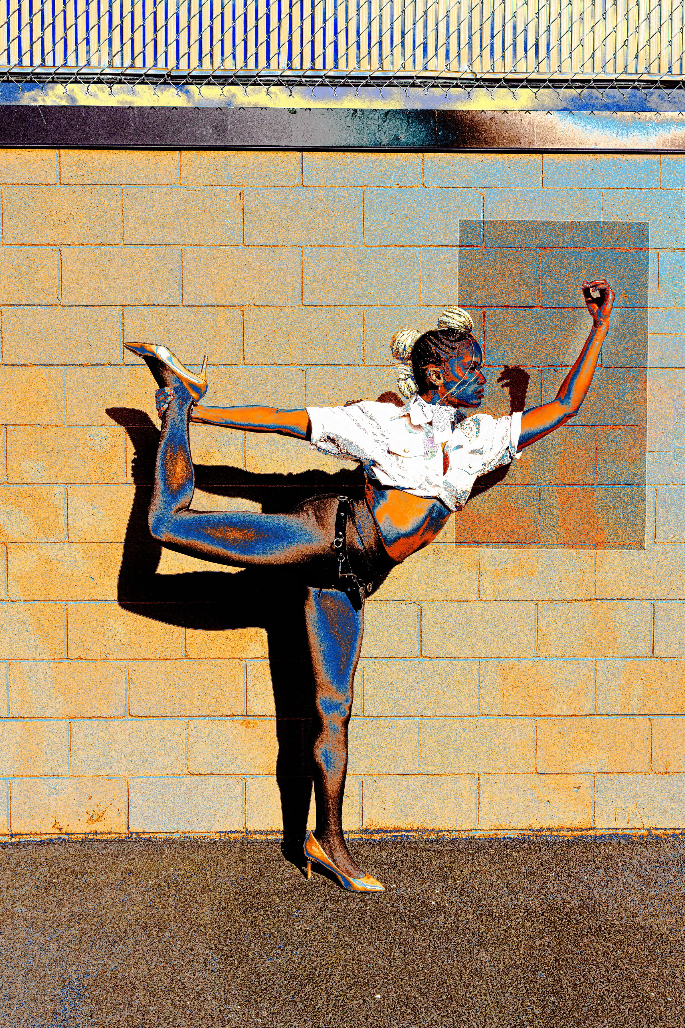 Person performing a handstand against a brick wall, wearing a white shirt and shorts, with one arm raised.