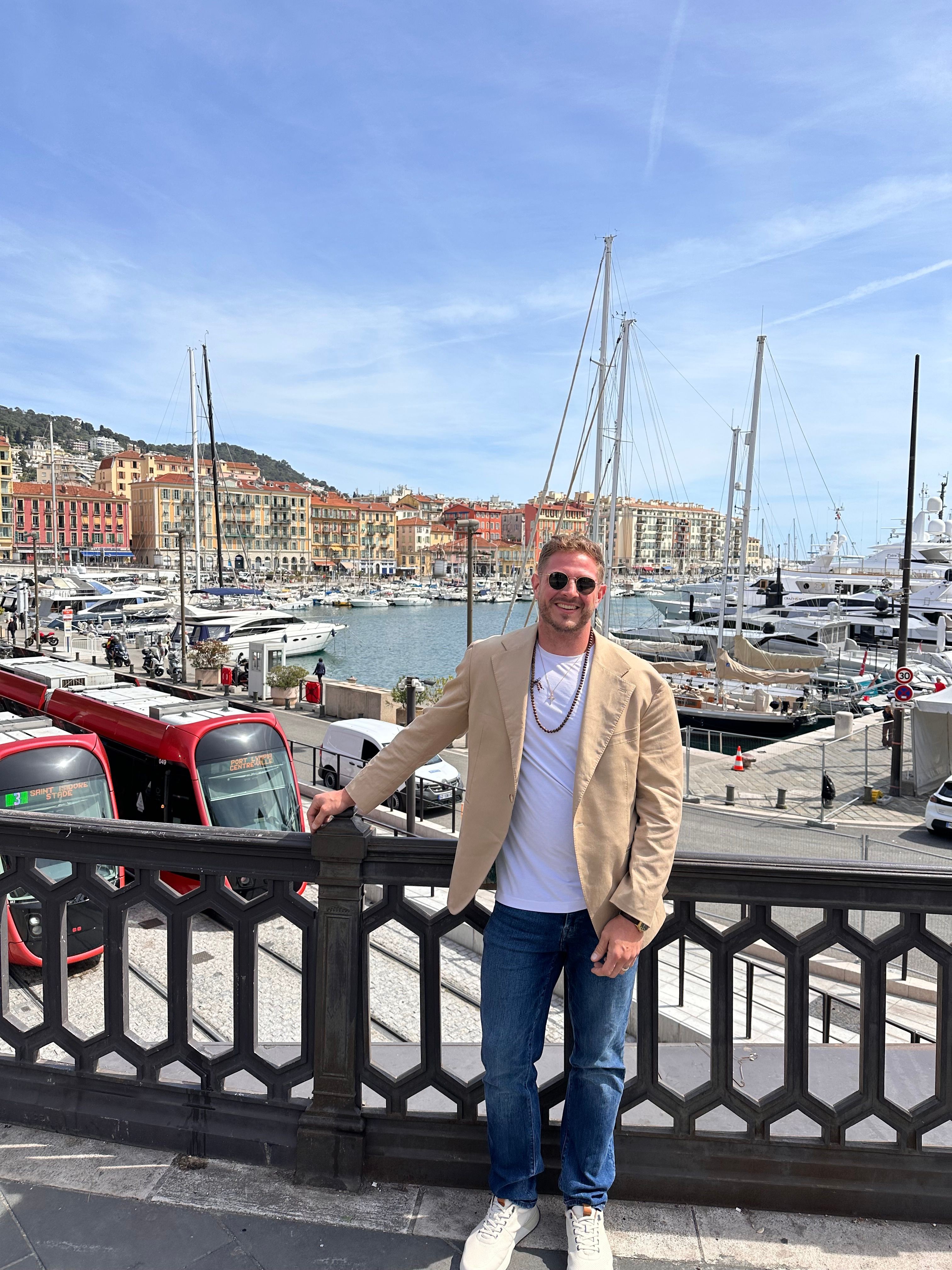 Person standing on a bridge with a marina and boats in the background, under a blue sky with clouds.