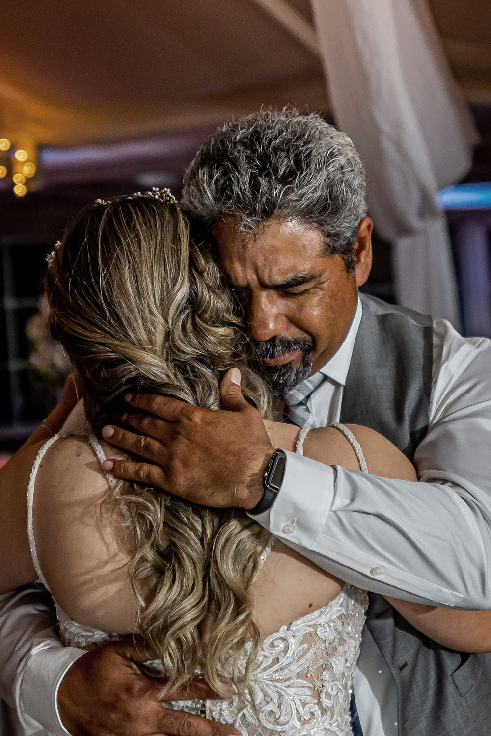 Man hugging woman, both with eyes closed, emotional moment, indoor setting with soft lighting
